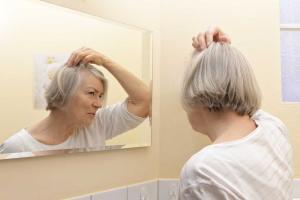 Woman with gray hair looking at her scalp in the mirror