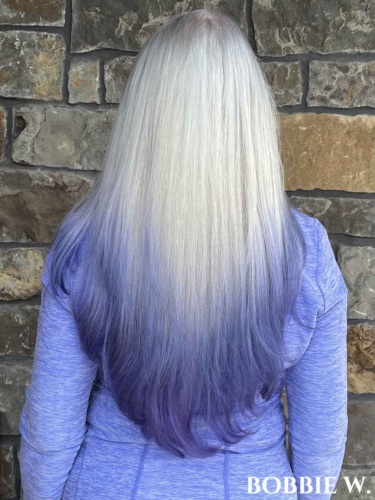 Woman facing away with long white hair and violet "ombre" dye on the ends.