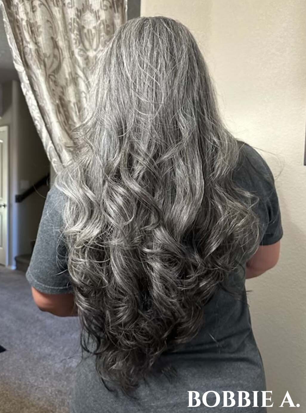 Woman facing away with waist length wavy dark silver hair.