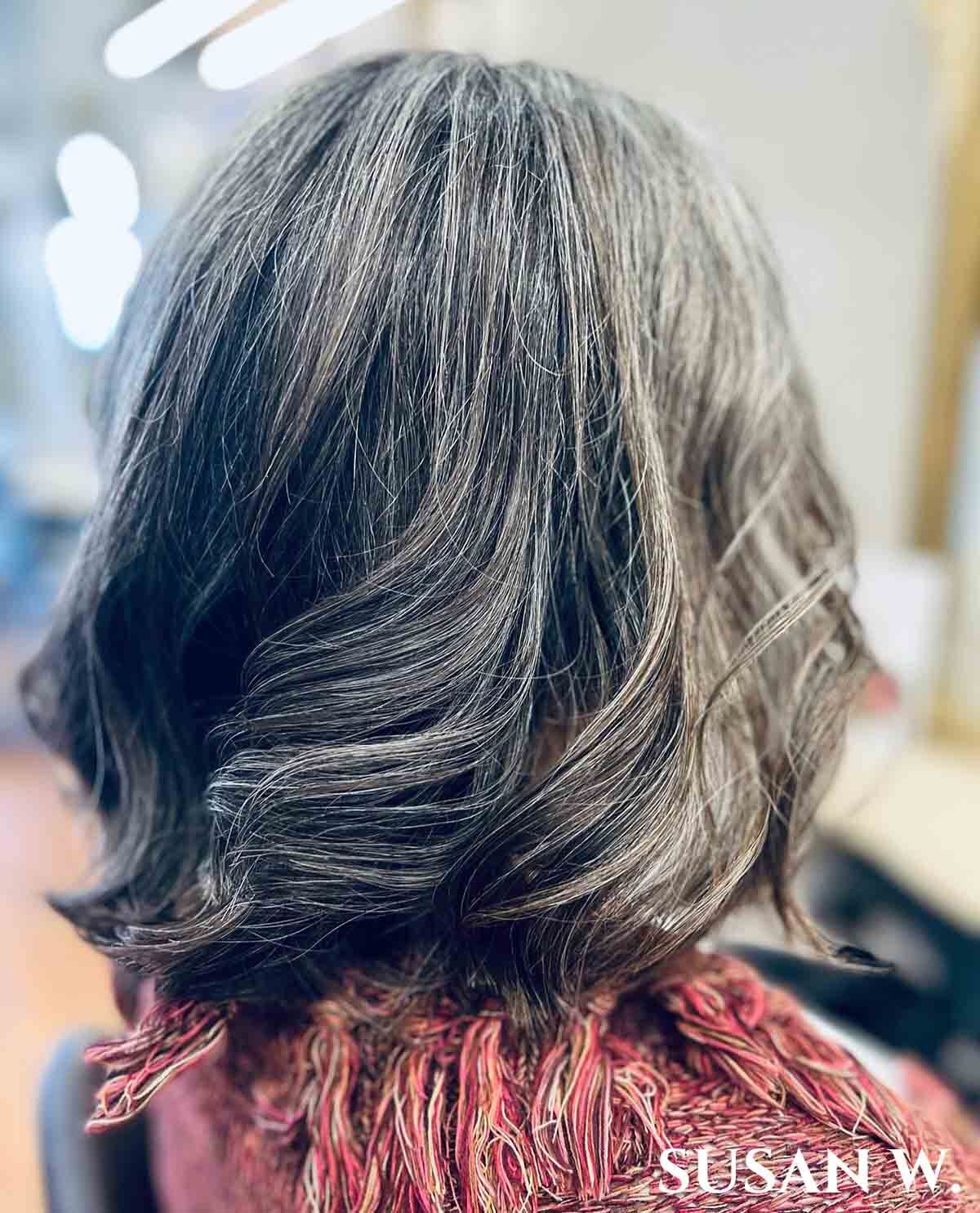 Woman facing away with above shoulder length curled dark silver hair.
