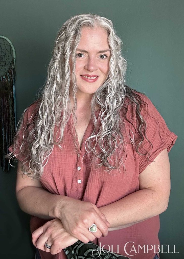 Author Joli Campbell with long silver wavy-curly hair.