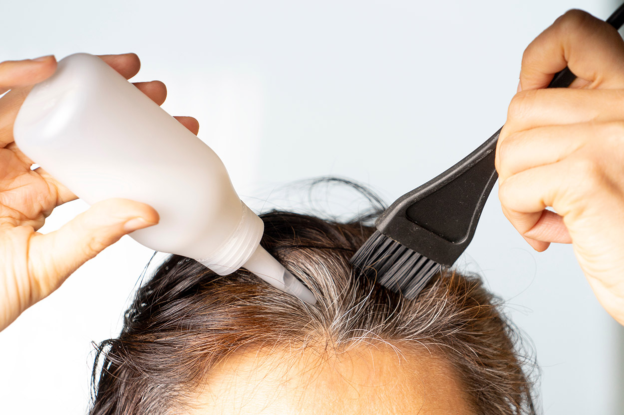 Closeup woman hands dyeing hair using black brush. Middle age woman colouring dark hair with gray roots at home.